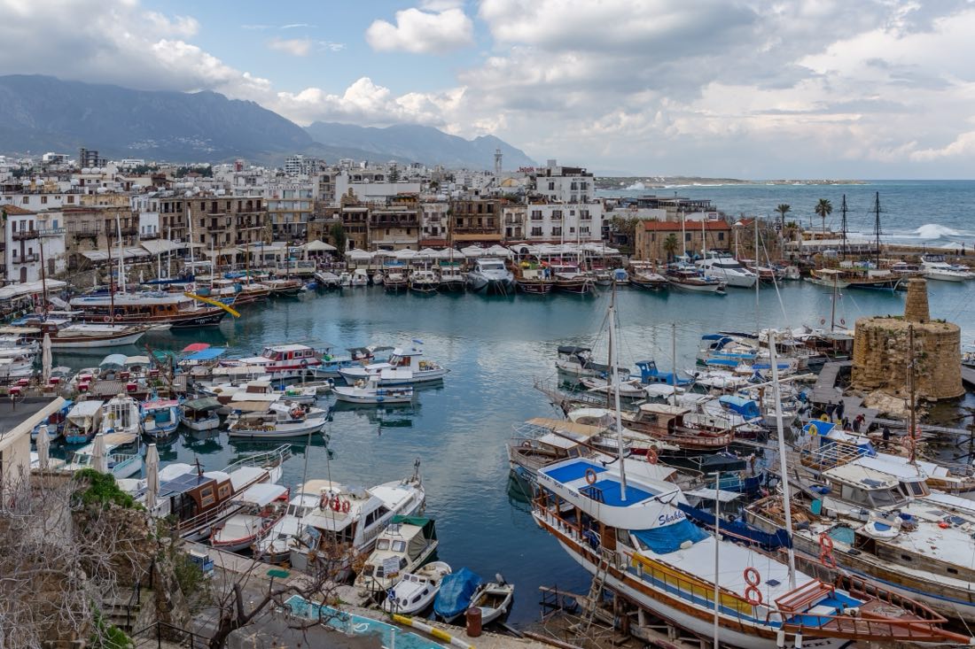 Kyrenia's old harbour with fishing and excursion boats, the stone buildings of the town behind, and the Kyrenia mountain range under a winter sky